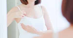 Close up of a woman touching her breasts through her white shirt, considering a breast augmentation