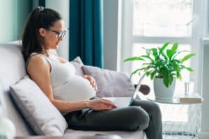 Pregnant woman sits on couch with enlarged breasts.